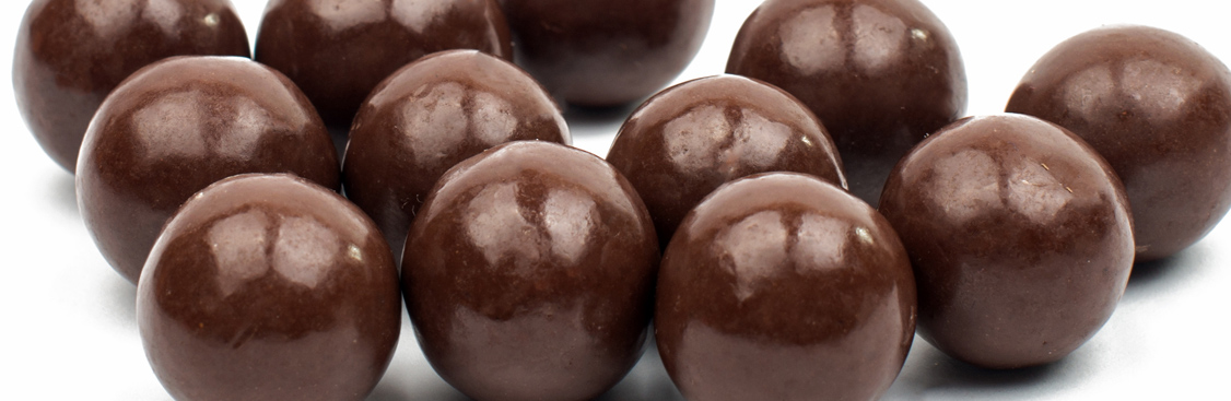 Silver spoon full of cocoa power leaning against broken pieces of chocolate bar