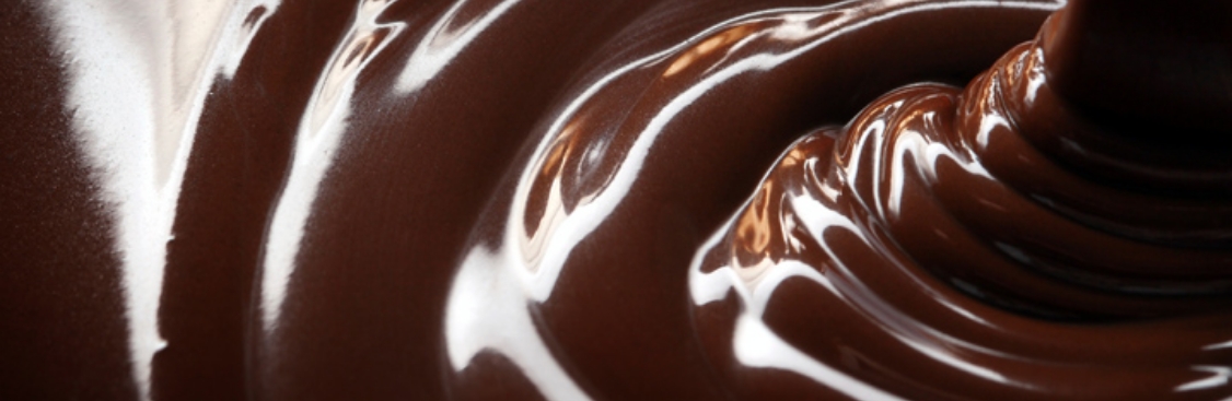 Silver spoon full of cocoa power leaning against broken pieces of chocolate bar