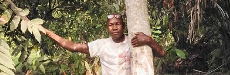 Photo of Guiemde Sidibé Alexandre grasping a tree in a forest setting